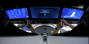 A view inside the SpaceX Dragon space capsule showing astronauts in front of cockpit display screens
